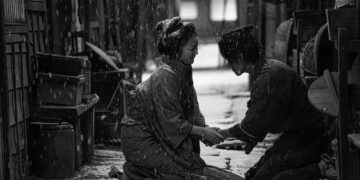 Haru Kuroki as Okiku kneeling on the ground in the street holding a man's hand as snow falls in the movie Okiku and the World.