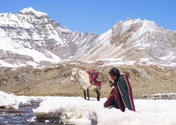 Thinley Lhamo as Pema kneeling in the snow in prayer by a river with a white horse behind her in the movie Shambhala.