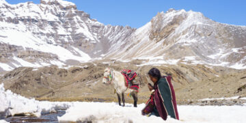 Thinley Lhamo as Pema kneeling in the snow in prayer by a river with a white horse behind her in the movie Shambhala.