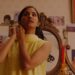 Amrit Kaur as Azra putting on an earring wearing a yellow dress in the movie The Queen of My Dreams.