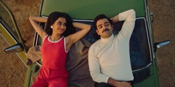 Amrit Kaur as Azra and Hamza Haq as Hassan laying next to each other on the hood of a green car in the Canadian movie The Queen of My Dreams