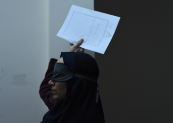 Mahsa Rostami as Rezvan blind folded and holding a piece of paper above her head in The Seed of the Sacred Fig.