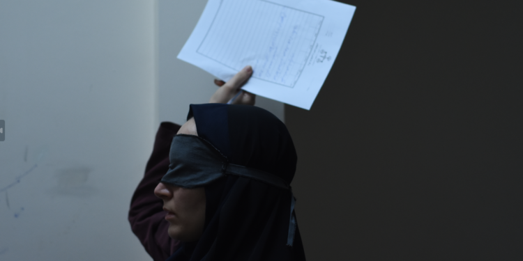 Mahsa Rostami as Rezvan blind folded and holding a piece of paper above her head in The Seed of the Sacred Fig.
