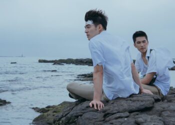 Edward Chen as Chang Jia-han and Jing-hua Tseng as Wong Po Te, sitting on a rocky beach, in Your Name Engraved Herein.