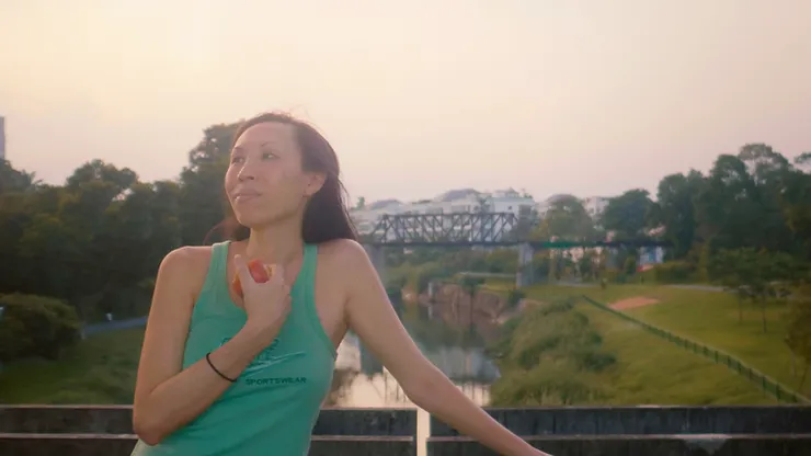 Quen Wong standing on a bridge holding an apple in the documentary Some Women.
