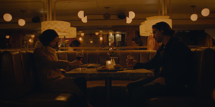 Andrea Bang as Grace and Joe Scarpellino as Carter sitting across from each other in a dimly lit restaurant in Stay the Night.