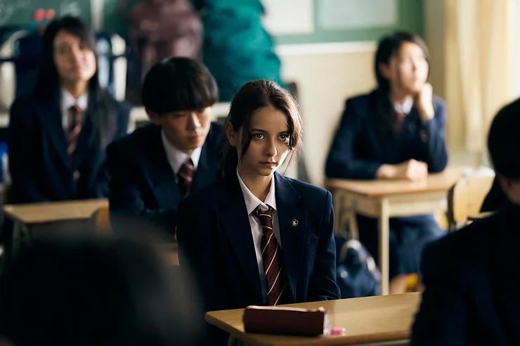 Arashi Lina as Sarya sitting at her desk in a high school class room in My Small Land.