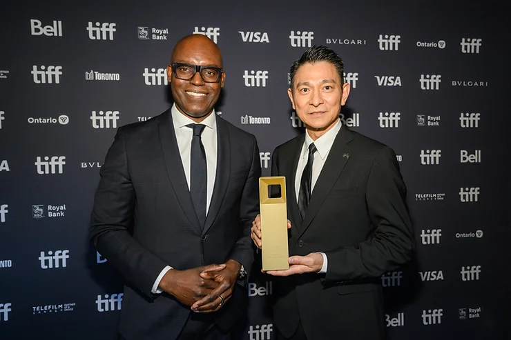 Cameron Bailey and Andy Lau holding an award posing on the TIFF red carpet