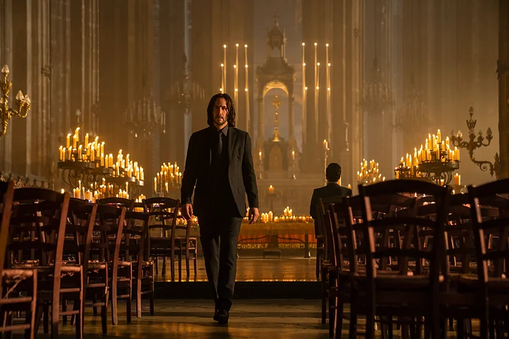 Keanu Reeves as John Wick walking through a church wearing a black suit like a bad ass in the movie John Wick: Chapter 4.