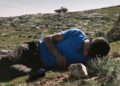 A young man laying on his side on a hill from the documentary No Other Land.