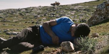 A young man laying on his side on a hill from the documentary No Other Land.