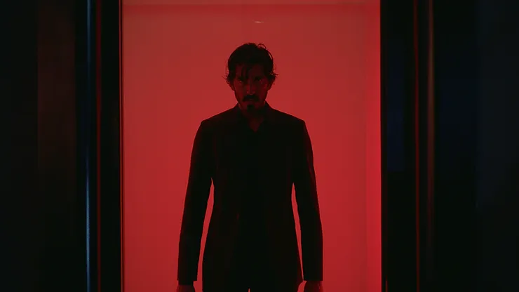 Dev Patel as Kid walking through a doorway with red light behind him in Monkey Man.