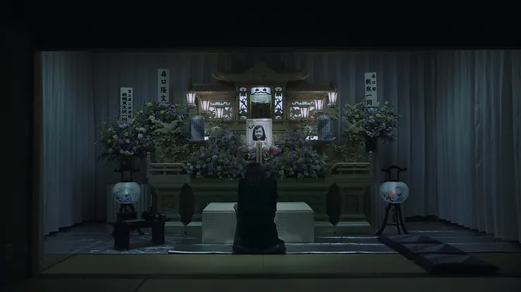 A traditional Japanese death shrine with the picture of a young girl and a grieving woman kneeling in front wearing all black from Tetsuya Nakashima’s Confessions.