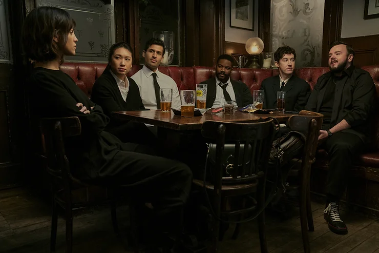 The ensemble cast of Three Body Problem sitting around a table in a booth.