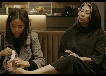 Sitting on a couch, Bayarjargal Bayartsetseg as Saruul wraps the big toe of Oidovjamts Enkhtuul as Katya in The Sales Girl