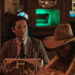 Jun Kunimura as Wada and Arata Iura as Hideki seated at a table in a cowboy bar opposite Robin Weigert as Peg in Tokyo Cowboy.