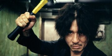 Choi Min-sik as Oh Dae-su wields a hammer in a hallway from Oldboy.
