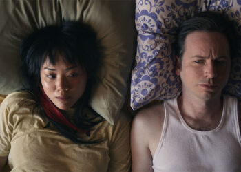 Emily Lê as Sonny and Dan Beirne as Chester laying side by side on a bed