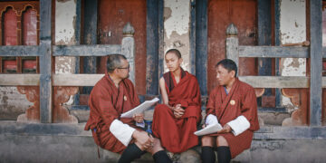 Three robed figures sit and discuss the happiness survey in Agent of Happiness documentary