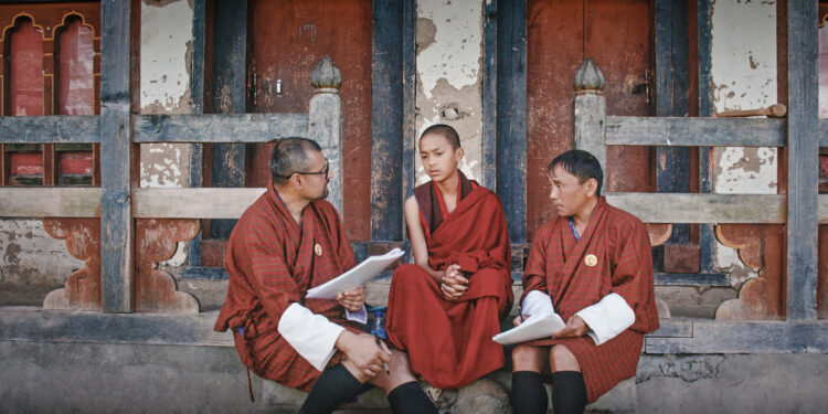 Three robed figures sit and discuss the happiness survey in Agent of Happiness documentary