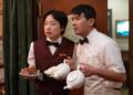 Jimmy O. Yang as Willis Wu and Ronny Chieng as Fatty Choi holding plates and tea pots in the television series Interior Chinatown.