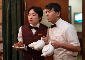 Jimmy O. Yang as Willis Wu and Ronny Chieng as Fatty Choi holding plates and tea pots in the television series Interior Chinatown.