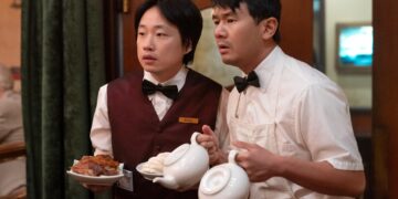 Jimmy O. Yang as Willis Wu and Ronny Chieng as Fatty Choi holding plates and tea pots in the television series Interior Chinatown.