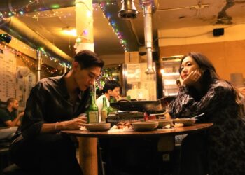 Kim Go-eun as Jae-hee and Steve Sanghyun Noh as Heung-soo sit in a dimly lit Korean restaurant in Love in the Big City.