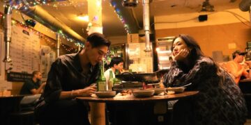 Kim Go-eun as Jae-hee and Steve Sanghyun Noh as Heung-soo sit in a dimly lit Korean restaurant in Love in the Big City.