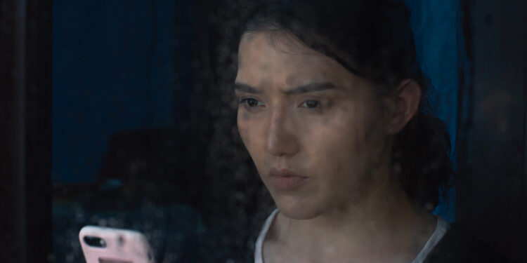 Guzalnur Uchqun in Nikah staring out a window on a rainy day holding a mobile phone.