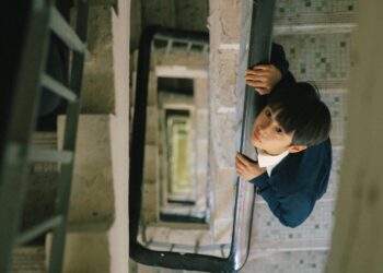 Curtis Ho Pak Lim as Alan looking up, standing in a stairwell in Time Still Turns the Pages