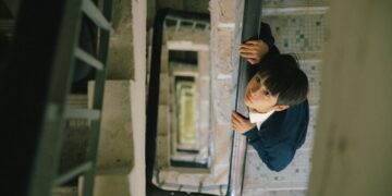 Curtis Ho Pak Lim as Alan looking up, standing in a stairwell in Time Still Turns the Pages