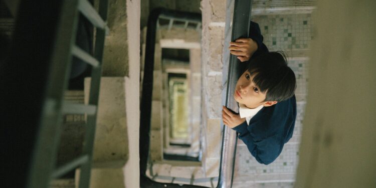 Curtis Ho Pak Lim as Alan looking up, standing in a stairwell in Time Still Turns the Pages