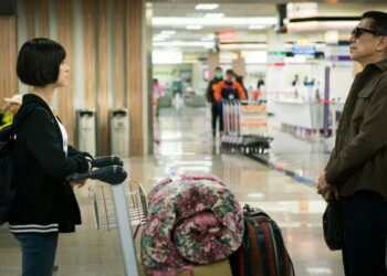 Ally Chiu as Shaowu stands across from Jack Kao as Keiko at an airport with a full luggage trolly between them in The Gangster's Daughter.