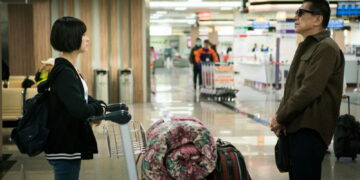 Ally Chiu as Shaowu stands across from Jack Kao as Keiko at an airport with a full luggage trolly between them in The Gangster's Daughter.