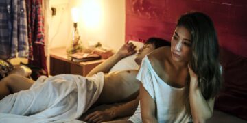 Rima Zeidan as Hsu Zi-qi sitting on the edge of a bed in Missing Johnny.