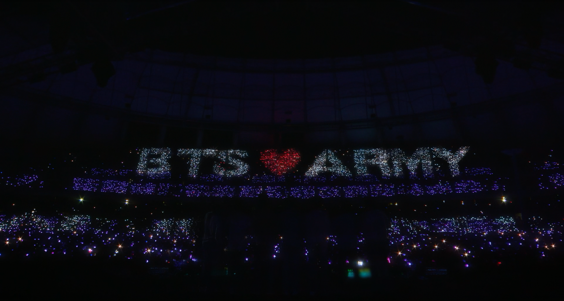 Fans spell out BTS ARMY in lights at a BTS concert. FOREVER WE ARE YOUNG directed by Grace Lee and Patty Ahn.