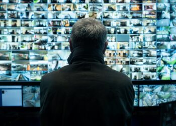 The back of a man's head watching a wall of surveillance videos in Stranger Eyes