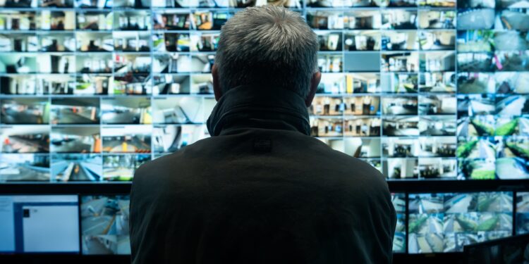 The back of a man's head watching a wall of surveillance videos in Stranger Eyes