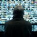 The back of a man's head watching a wall of surveillance videos in Stranger Eyes