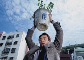 Lee Byung-hun as Yoo Man-su holding a flower pot over his head in No Other Choice