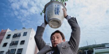 Lee Byung-hun as Yoo Man-su holding a flower pot over his head in No Other Choice