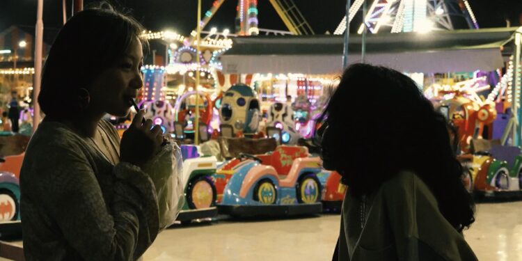 Sopheanith Thong and Deka Nine as Nisay and Thida in Whisperings of the Moon, having an intimate conversation at an amusement park.